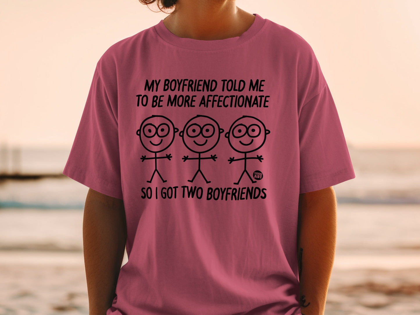 Pink t-shirt with text and stick figures: "My boyfriend told me to be more affectionate, so I got two boyfriends."