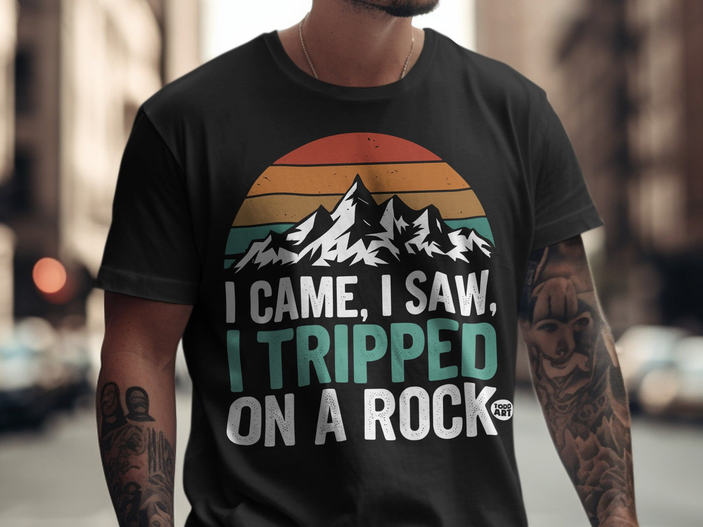 Black t-shirt with mountains, sunset graphic, and text "I came, I saw, I tripped on a rock."