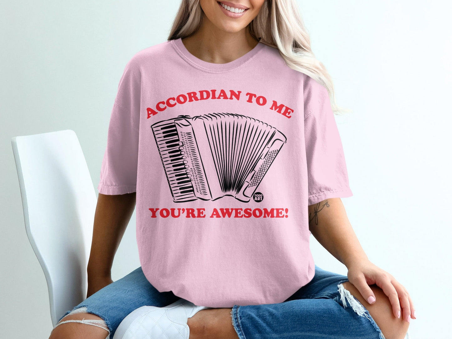 Pink t-shirt with a black accordion and text: ACCORDIAN TO ME YOU'RE AWESOME!