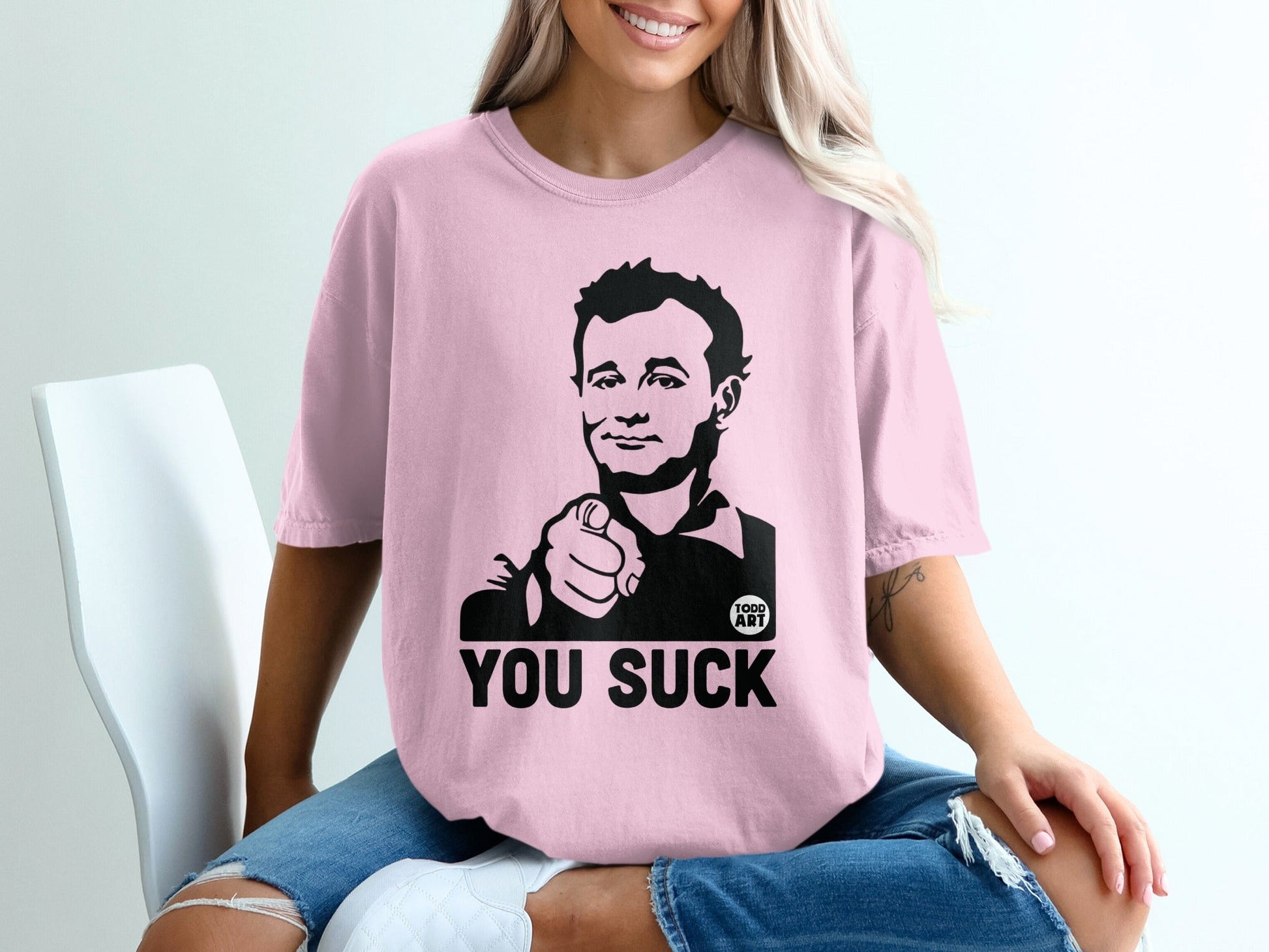 Pink t-shirt with black graphic of man pointing and text "YOU SUCK".
