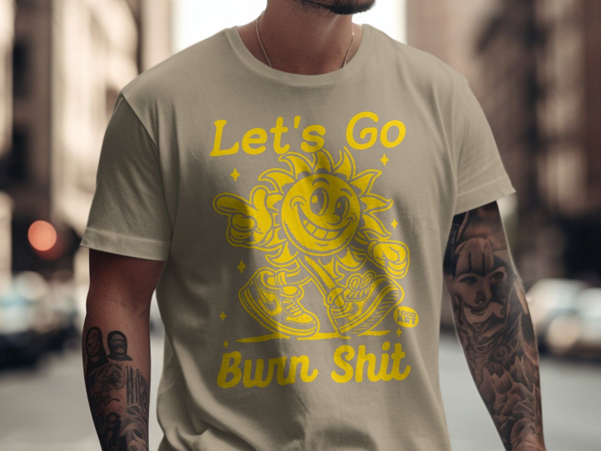 Tan t-shirt with yellow graphic of a sun saying "Let's Go Bwn Shit".