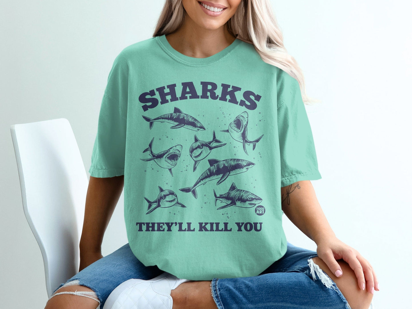 Teal t-shirt with purple graphic of various sharks and text "SHARKS THEY'LL KILL YOU".
