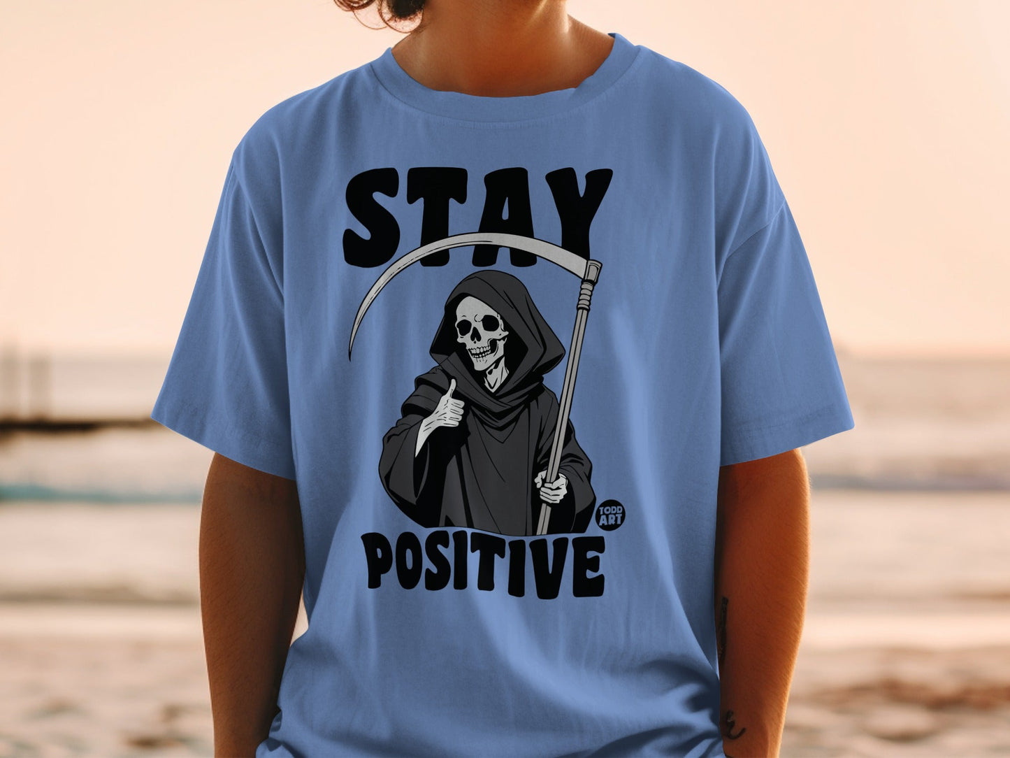 Blue t-shirt with Grim Reaper giving a thumbs up and "STAY POSITIVE" text.