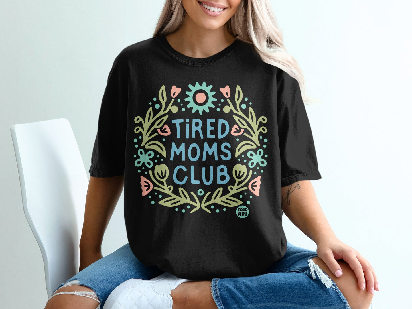 Black t-shirt with "TIRED MOMS CLUB" in a floral circle design.