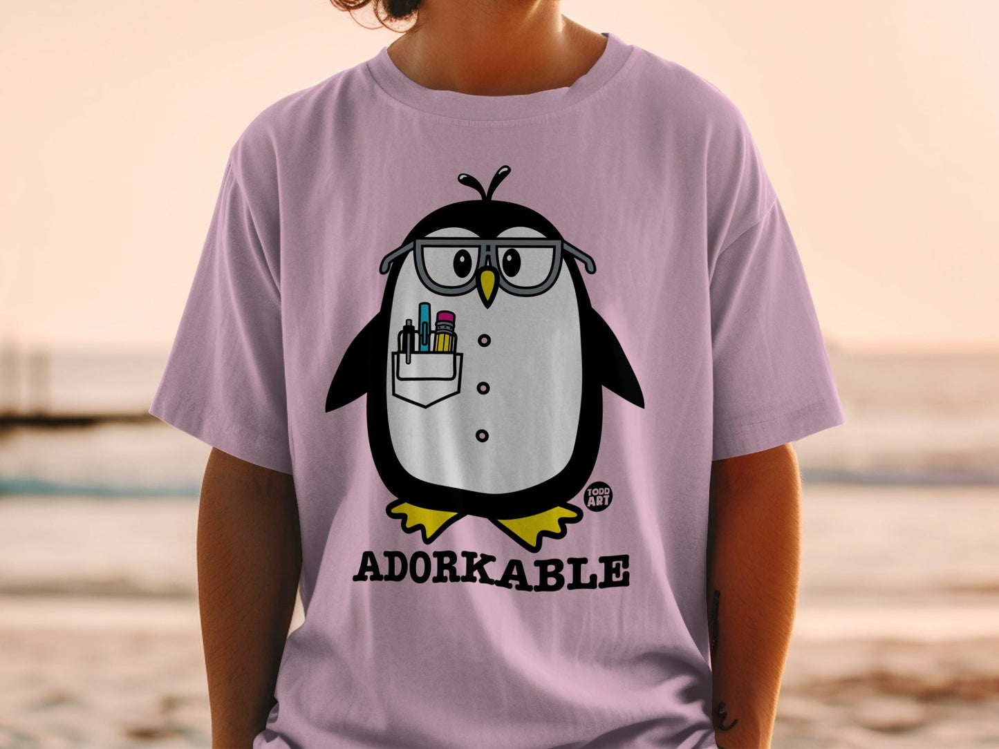 Pink t-shirt with cartoon penguin wearing glasses and holding pens.