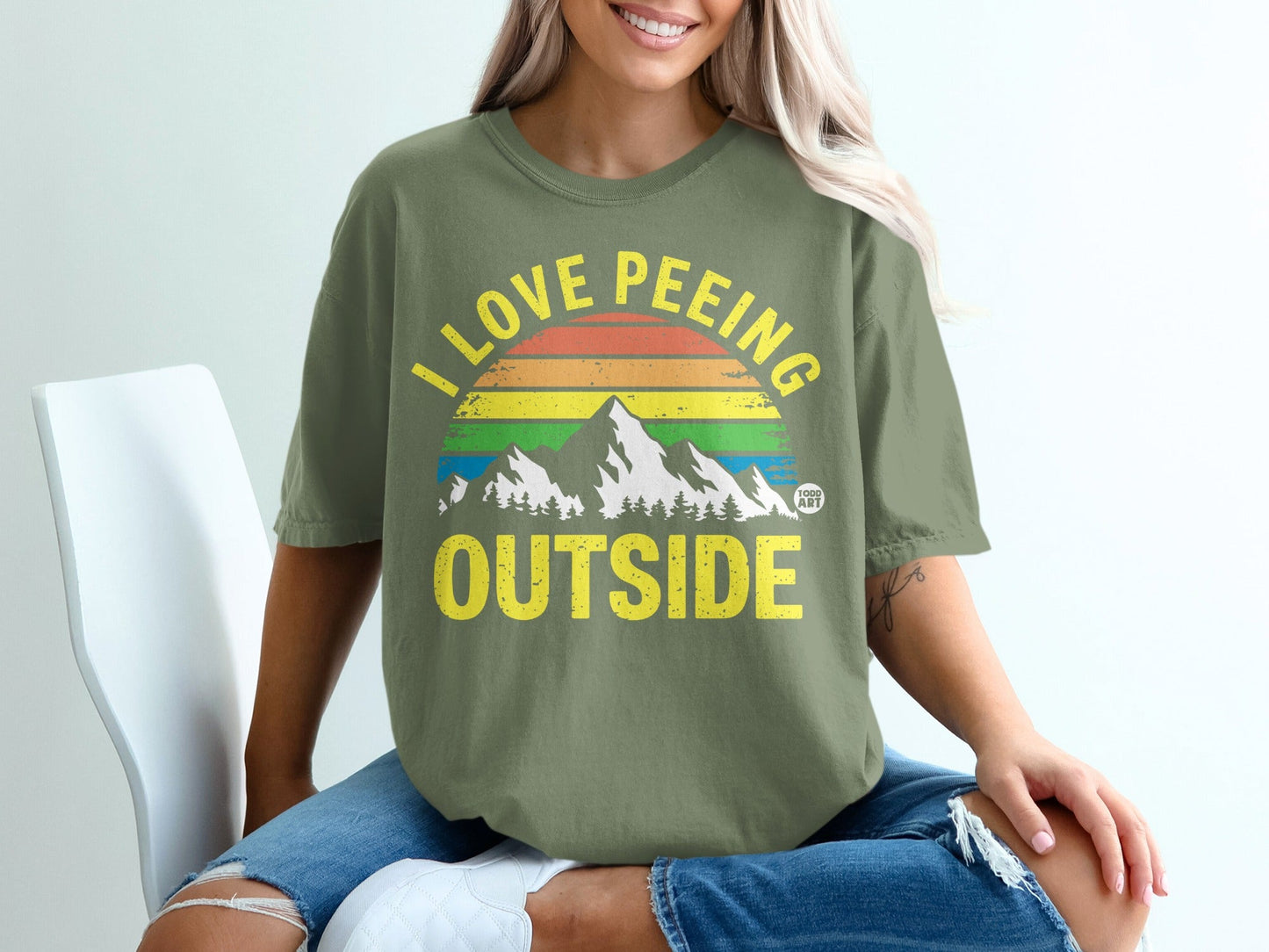 Olive green t-shirt with "I LOVE PE-EEING OUTSIDE" and rainbow mountain graphic.