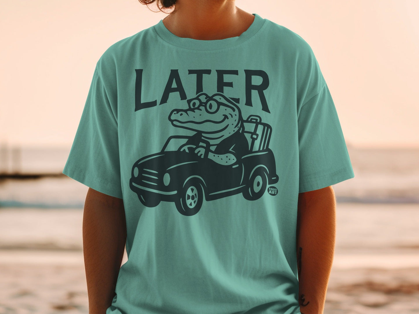 T-shirt with cartoon alligator driving a car with sunglasses.
