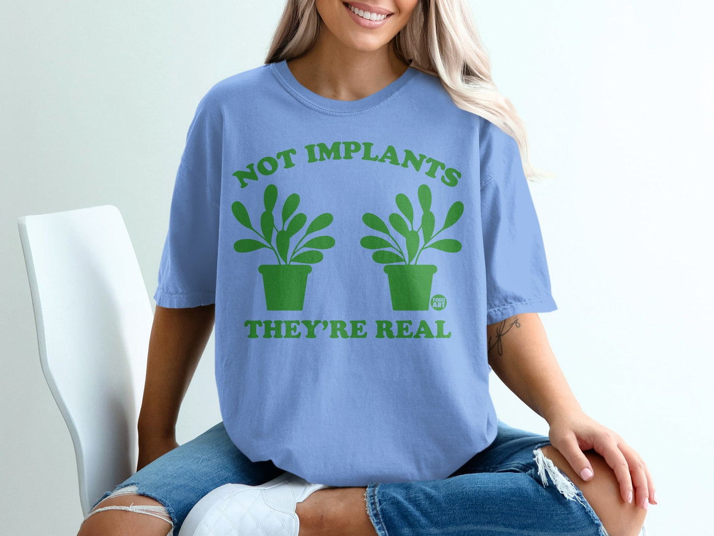 Blue t-shirt with green text "NOT IMPLANTS THEY'RE REAL" and potted plants.