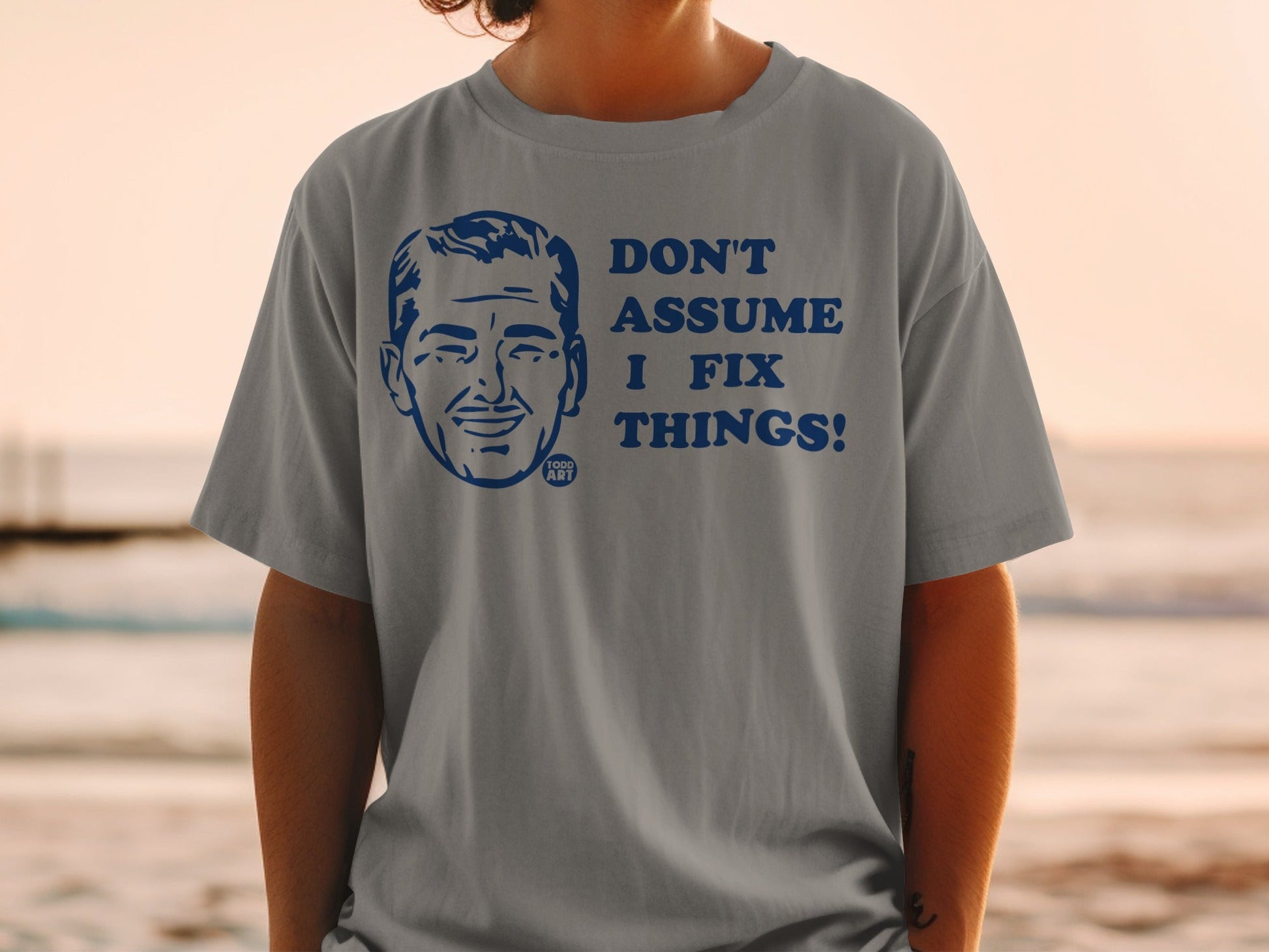 Grey t-shirt with "DON'T ASSUME I FIX THINGS!" and a cartoon man.