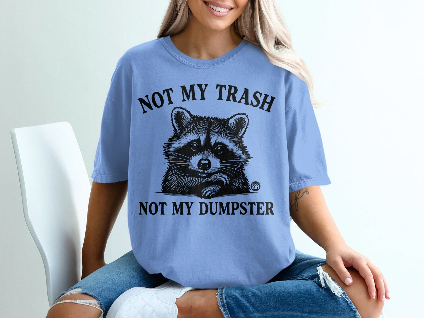 Light blue t-shirt with raccoon graphic and text "NOT MY TRASH NOT MY DUMPSTER".