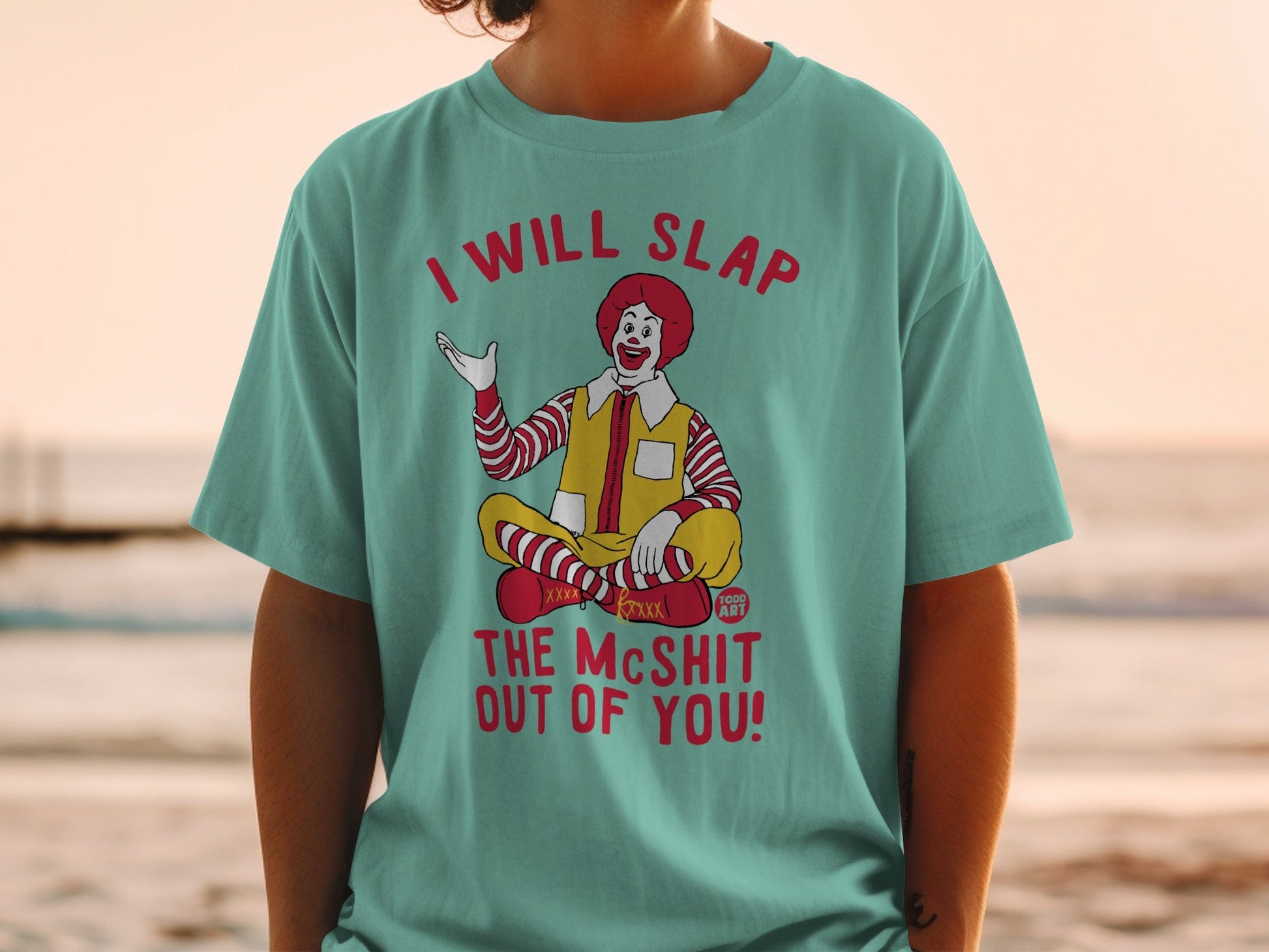Ronald McDonald sitting cross-legged, wearing a teal t-shirt with text.