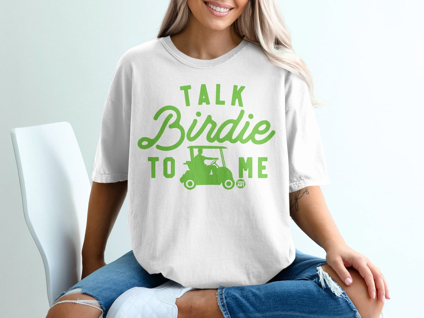White t-shirt with green text and golf cart graphic saying "Talk Birdie To Me".