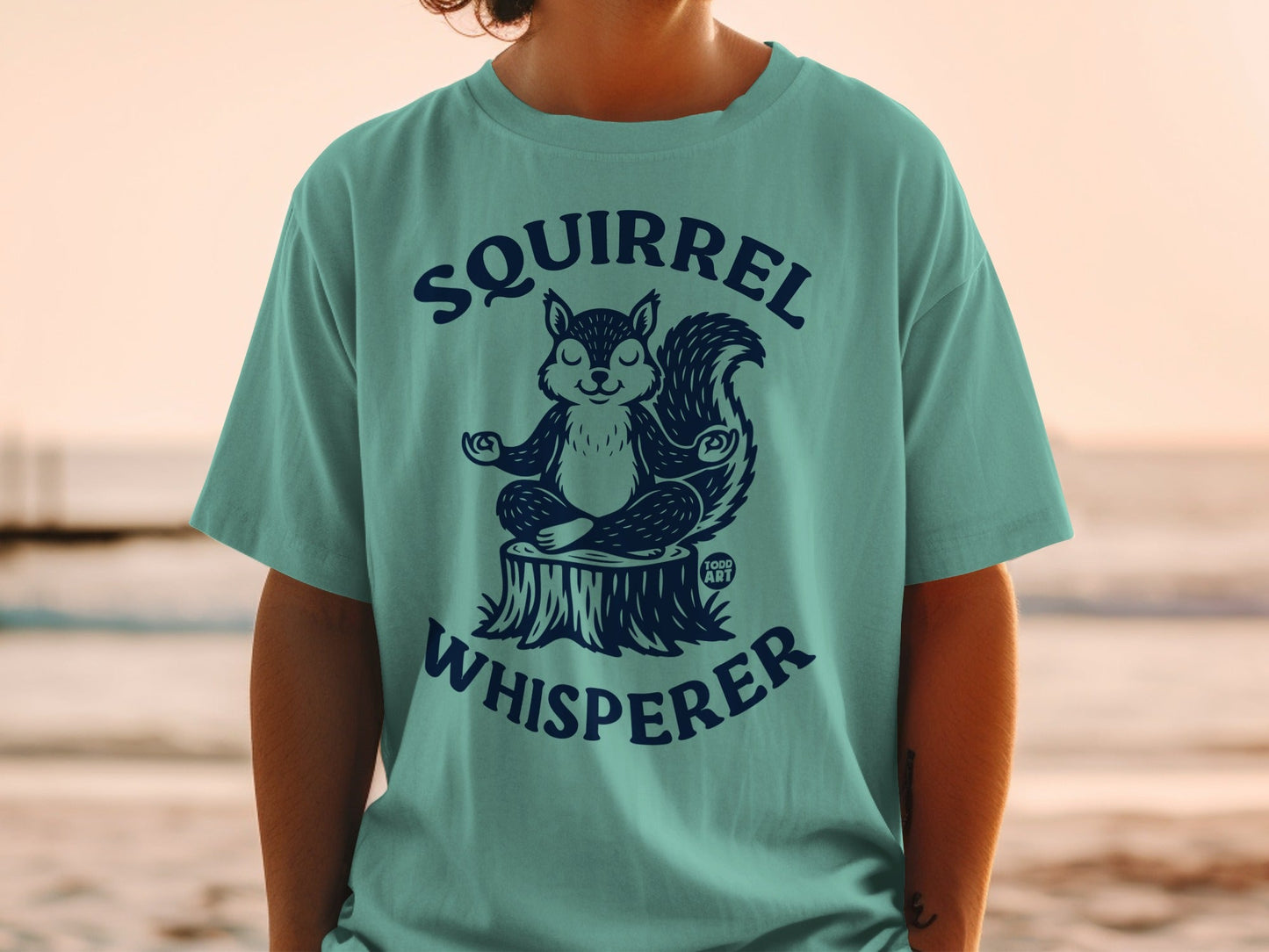 Teal t-shirt with a meditating squirrel on a tree stump, "Squirrel Whisperer" text.