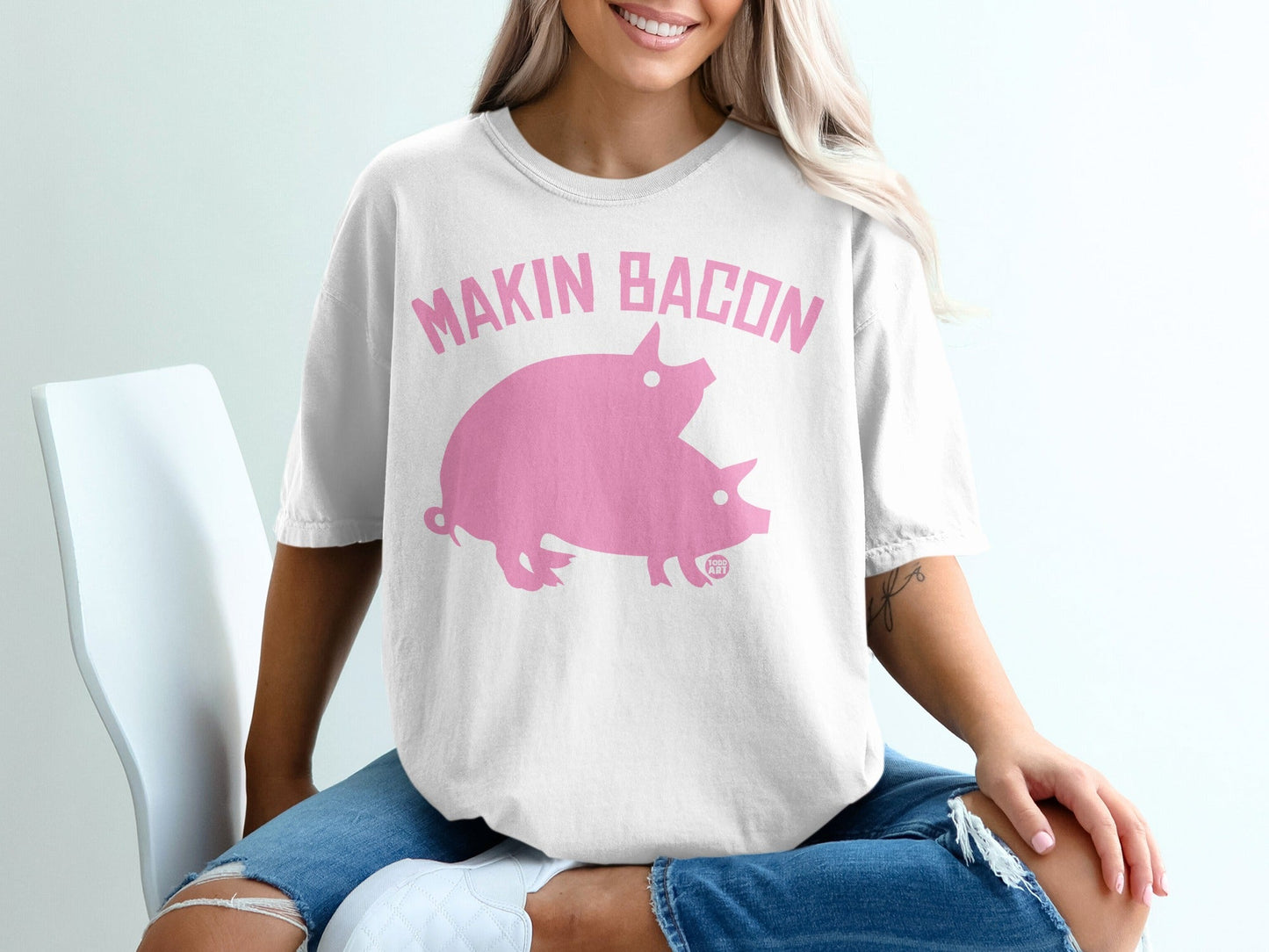 White t-shirt with pink text "MAKIN BACON" and two pink pigs.
