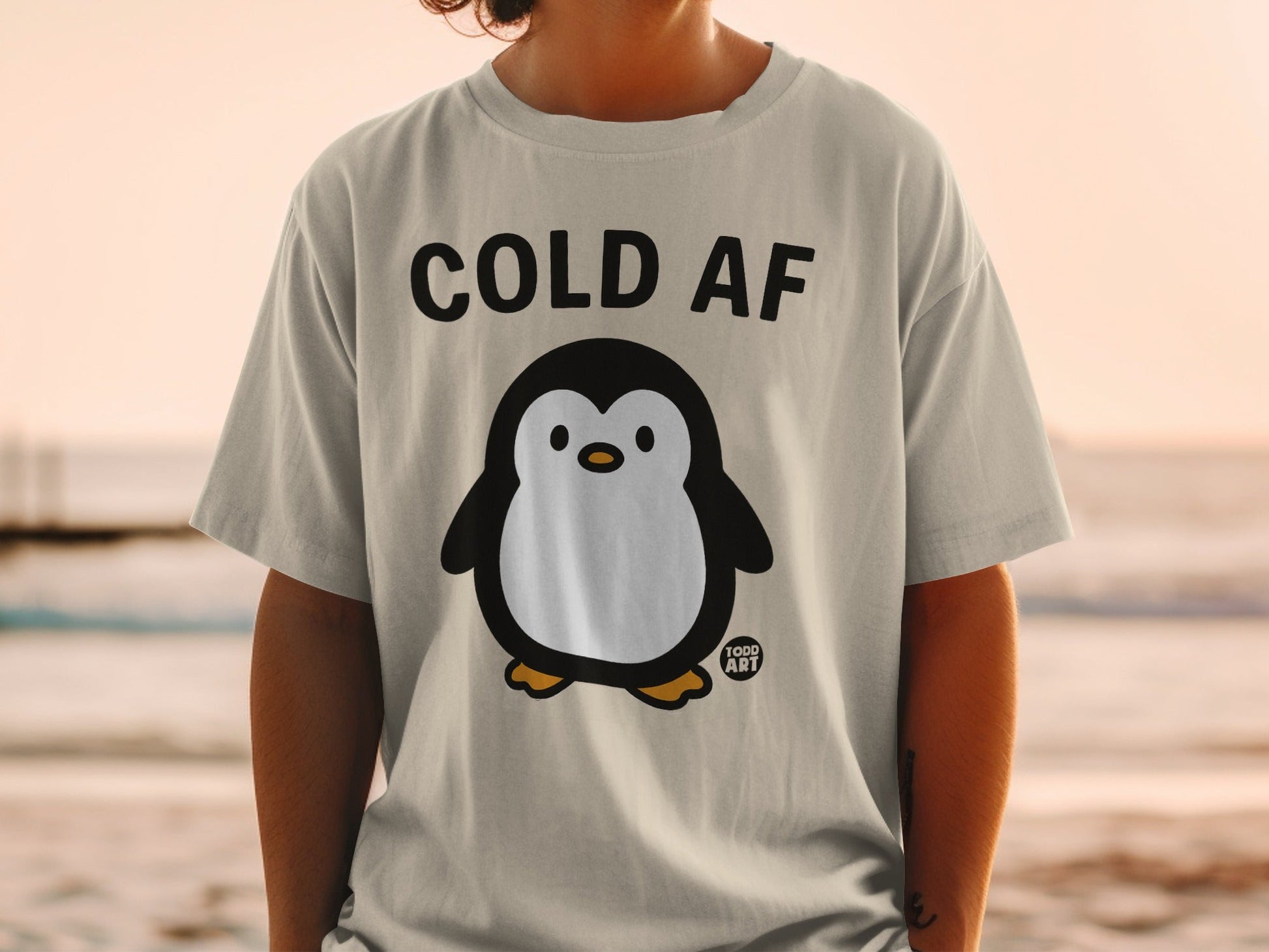 Light grey t-shirt with a cartoon penguin and text "COLD AF" and "TODD ART".