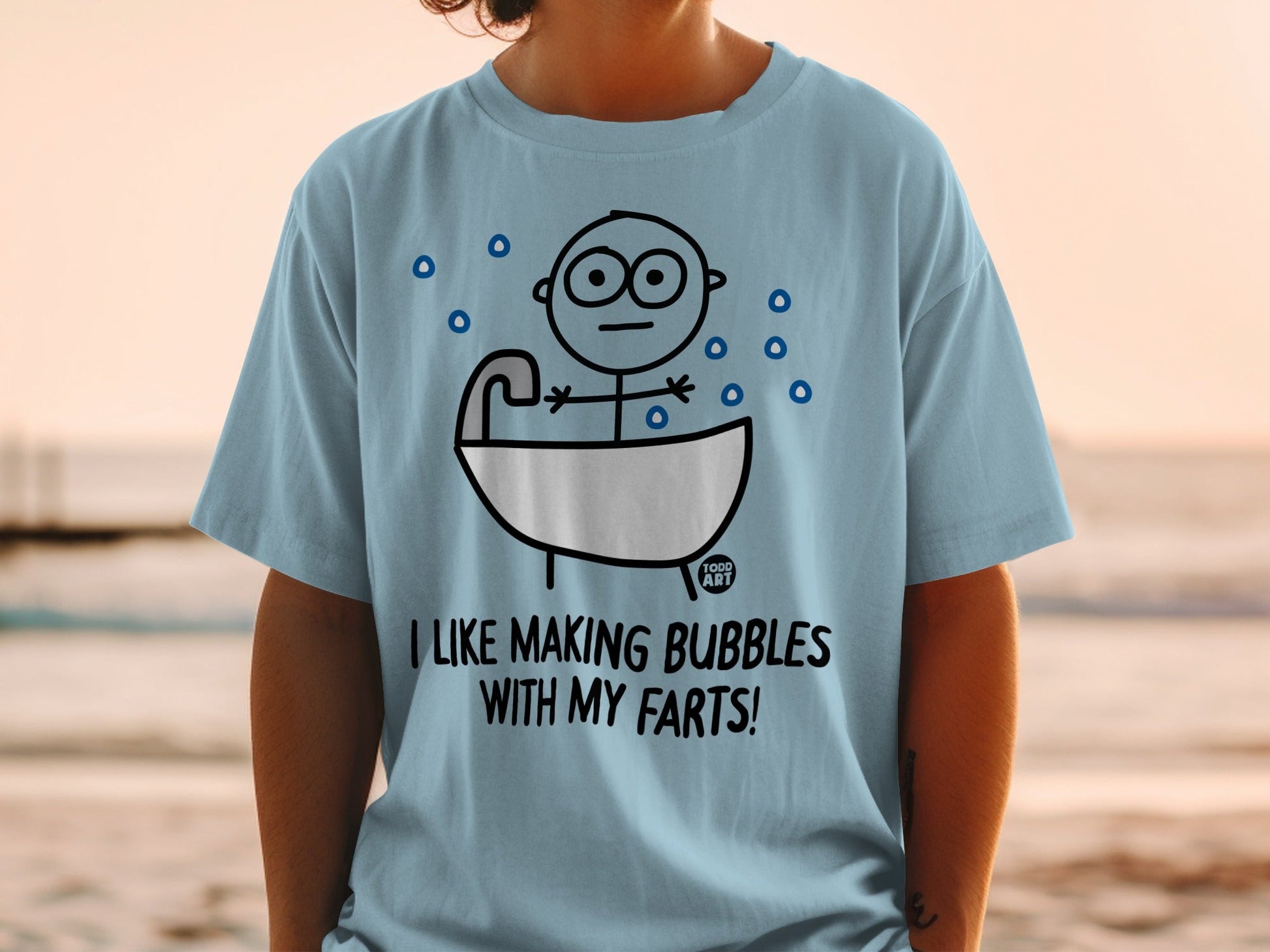 Light blue t-shirt with cartoon character in bathtub and text "I LIKE MAKING BUBBLES WITH MY FARTS!".
