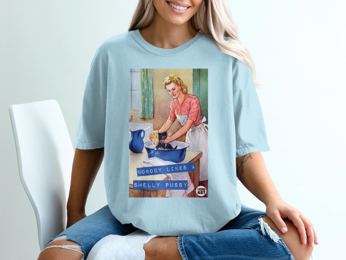 Light blue t-shirt with retro graphic of woman washing cat, text "NOBODY LIKES A SMELLY PUSSY".