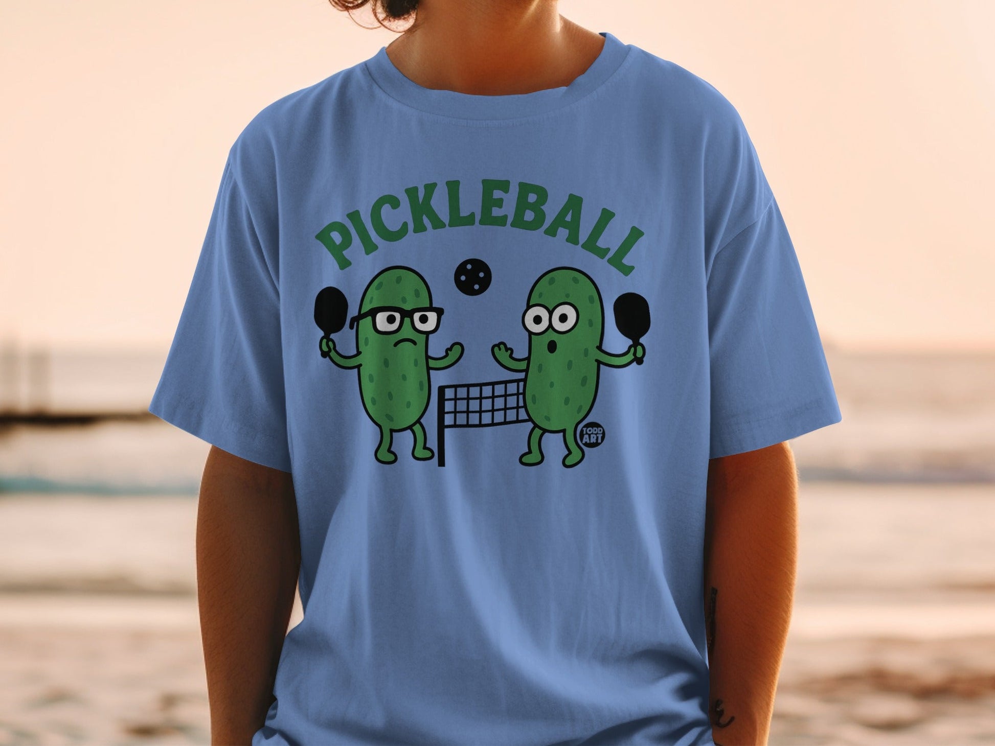 Two cartoon pickles playing pickleball with paddles and a net.