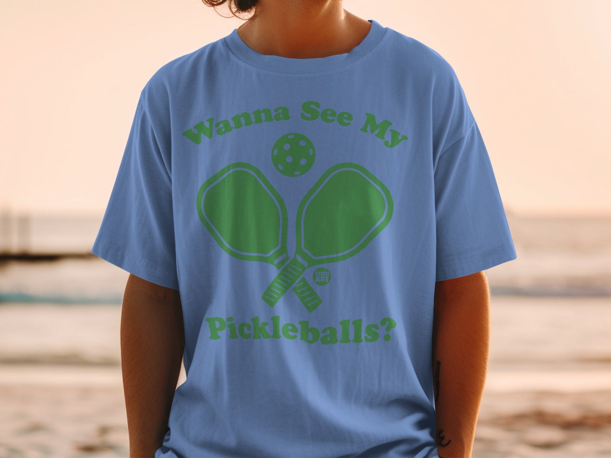 Blue t-shirt with green graphic of pickleball paddles and ball with text "Wanna See My Pickleballs?".