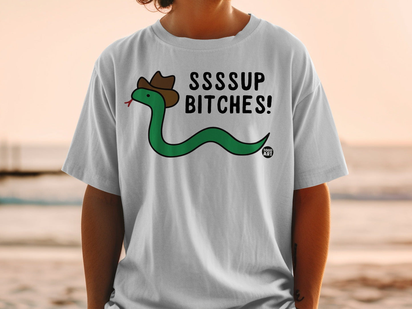 Green snake in a cowboy hat wearing a white t-shirt that says "SSSSUP BITCHES!"