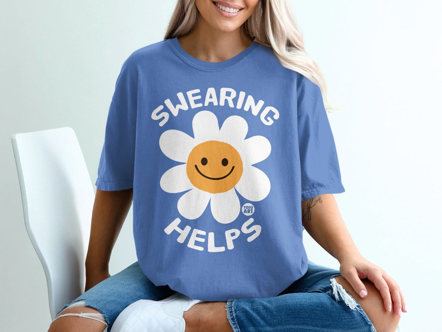 Blue t-shirt with a white daisy graphic and "SWEARING HELPS" text.