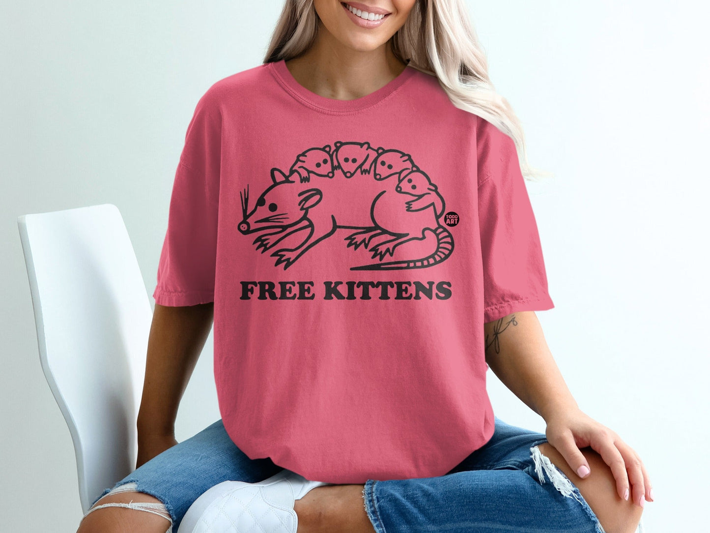 Pink t-shirt with a black line drawing of a rat carrying several kittens.