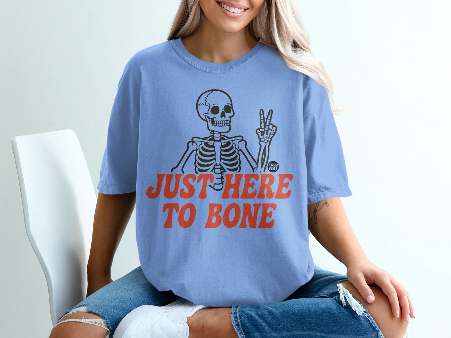 Light blue t-shirt with skeleton graphic and "JUST HERE TO BONE" text.