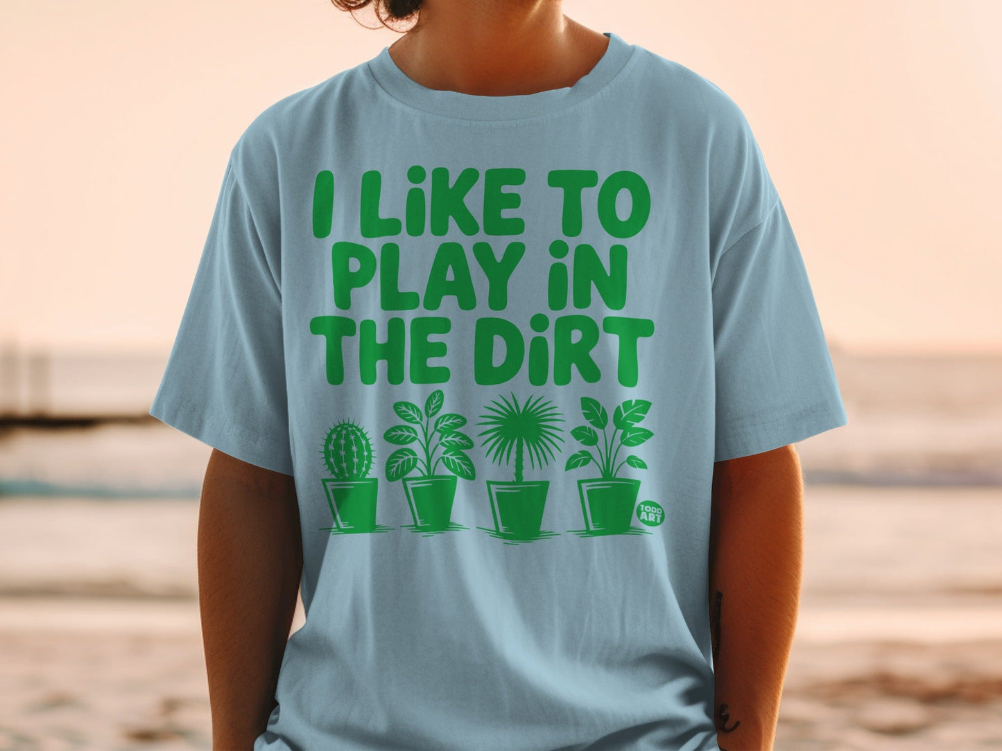 Light blue t-shirt with green text "I LIKE TO PLAY IN THE DIRT" and potted plants.