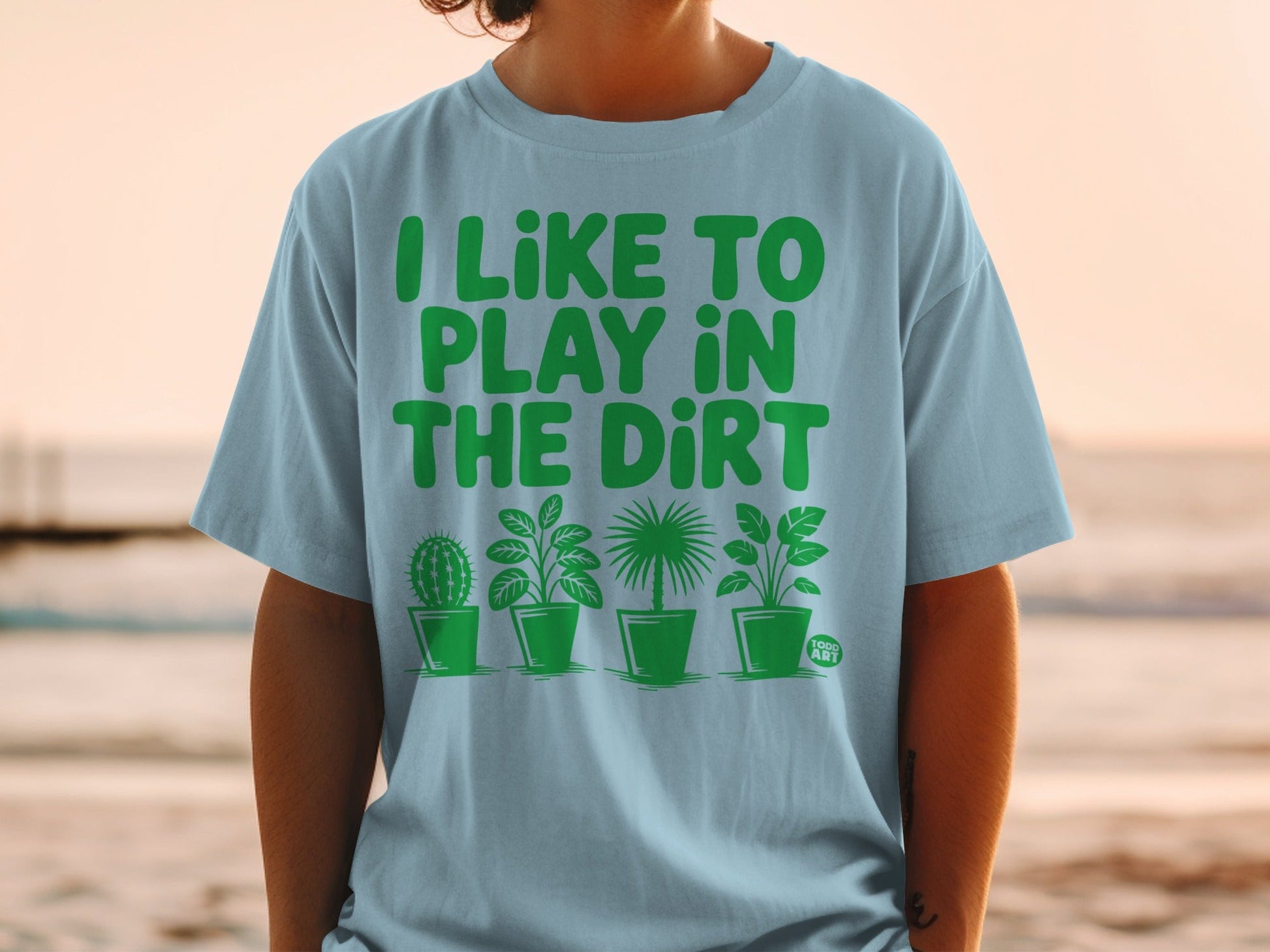 Light blue t-shirt with green text "I LIKE TO PLAY IN THE DIRT" and potted plants.