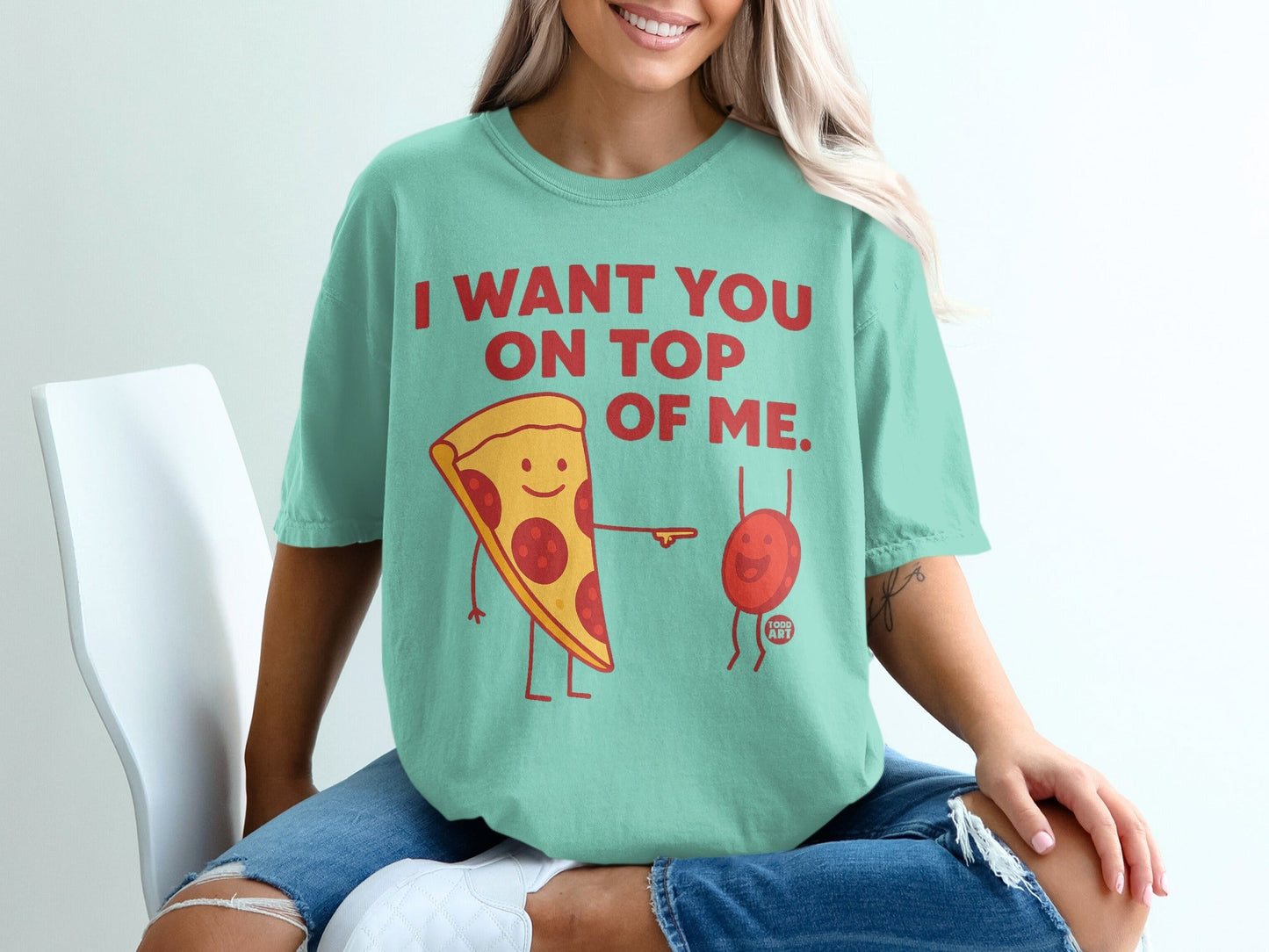 Teal t-shirt with pizza and a small red character saying "I want you on top of me".