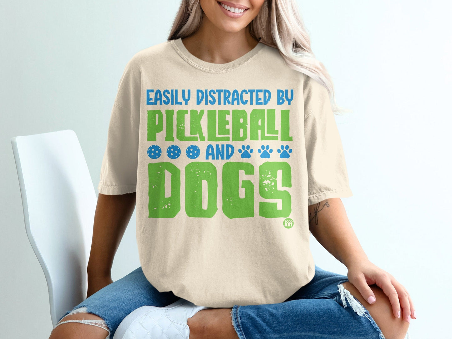 T-shirt with text "Easily distracted by pickleball and dogs" in green and blue.