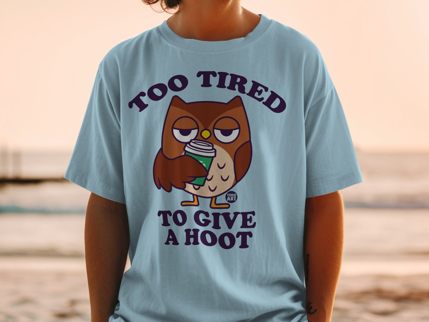 Light blue t-shirt with an owl holding a coffee cup and the text "Too tired to give a hoot."
