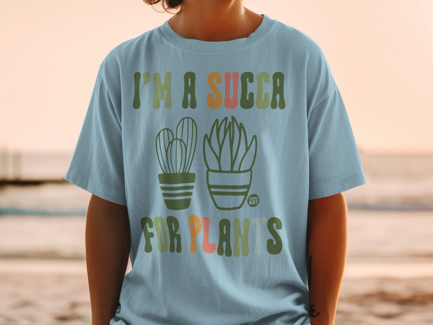 Green and orange text and cacti graphic on a light blue t-shirt.