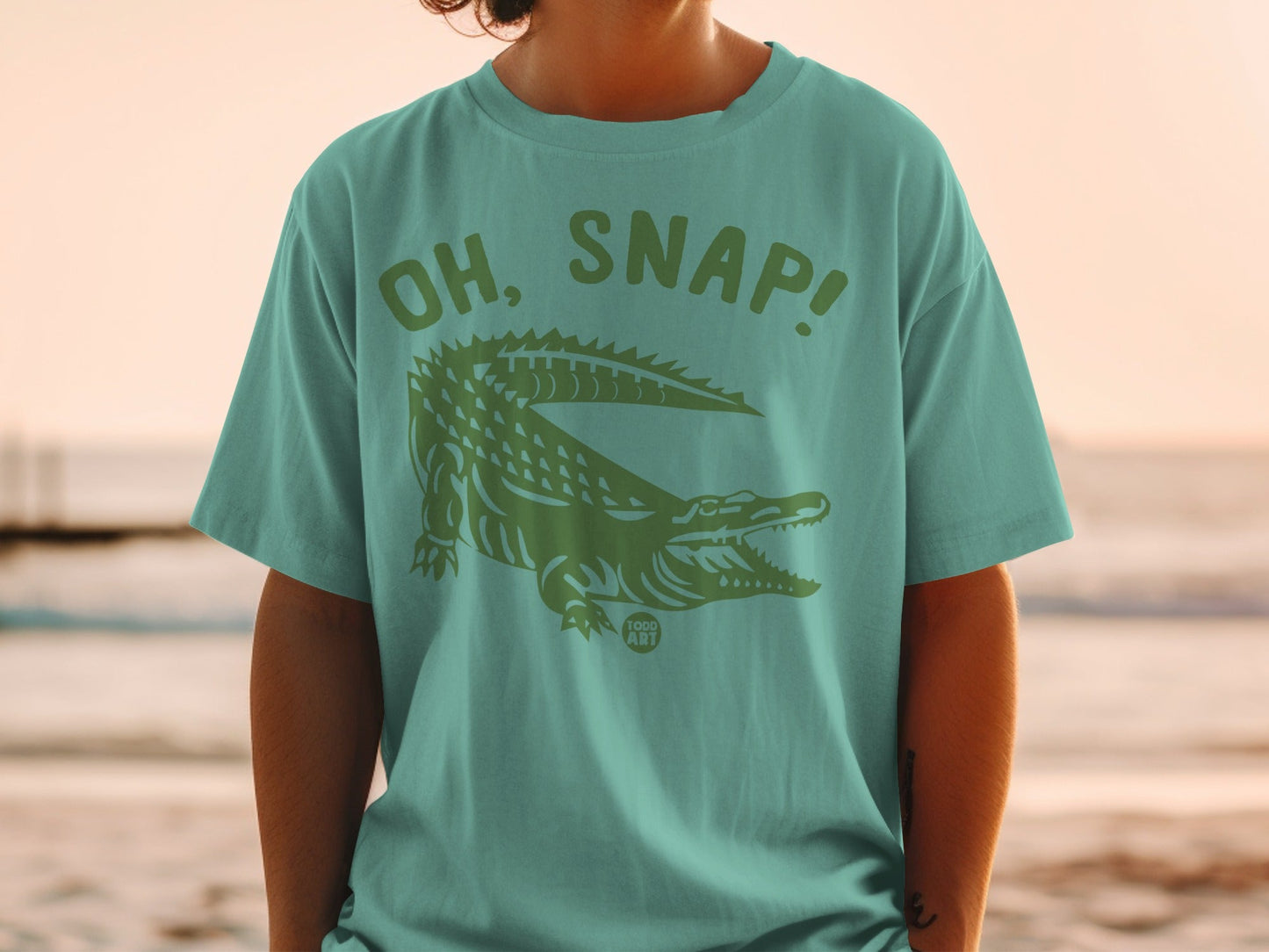 Green t-shirt with "OH, SNAP!" and alligator graphic, "1000 ART" logo.
