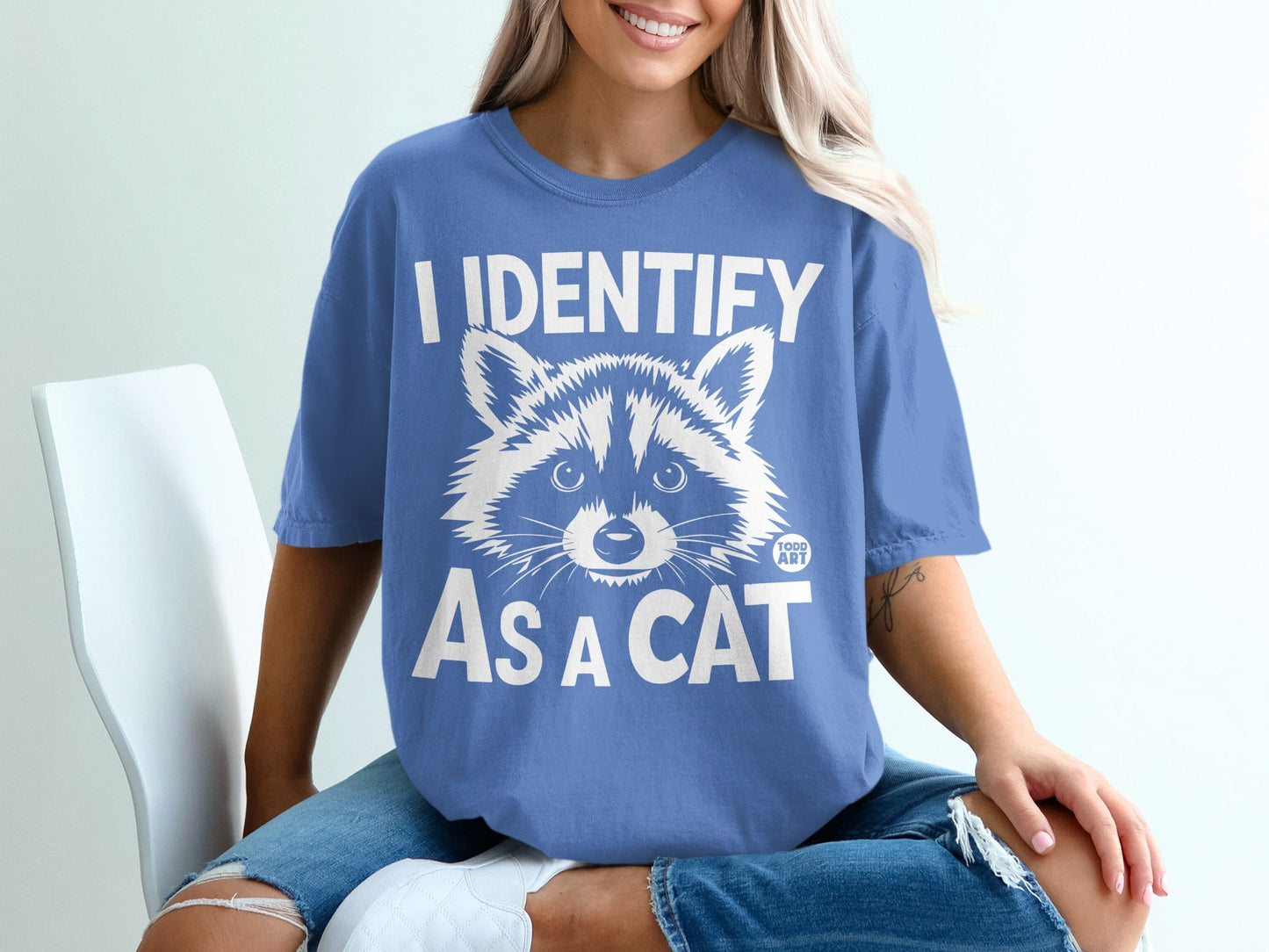 Blue t-shirt with white text "I IDENTIFY AS A CAT" and raccoon graphic.