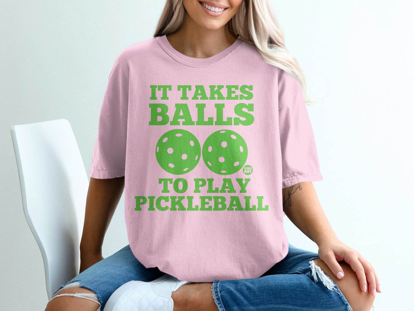 Pink t-shirt with green text and pickleball graphics that says "It Takes Balls To Play Pickleball".