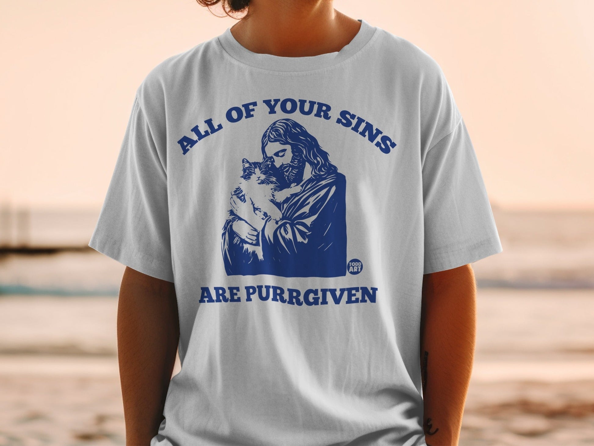 White t-shirt with Jesus holding a cat, text reads "All of your sins are purrgiven".