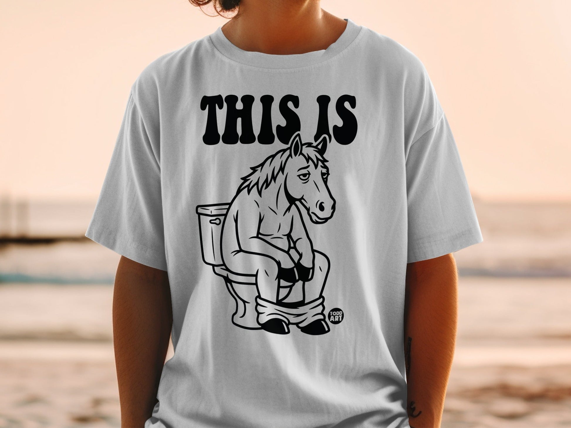 T-shirt with text "THIS IS" and illustration of a horse sitting on a toilet.