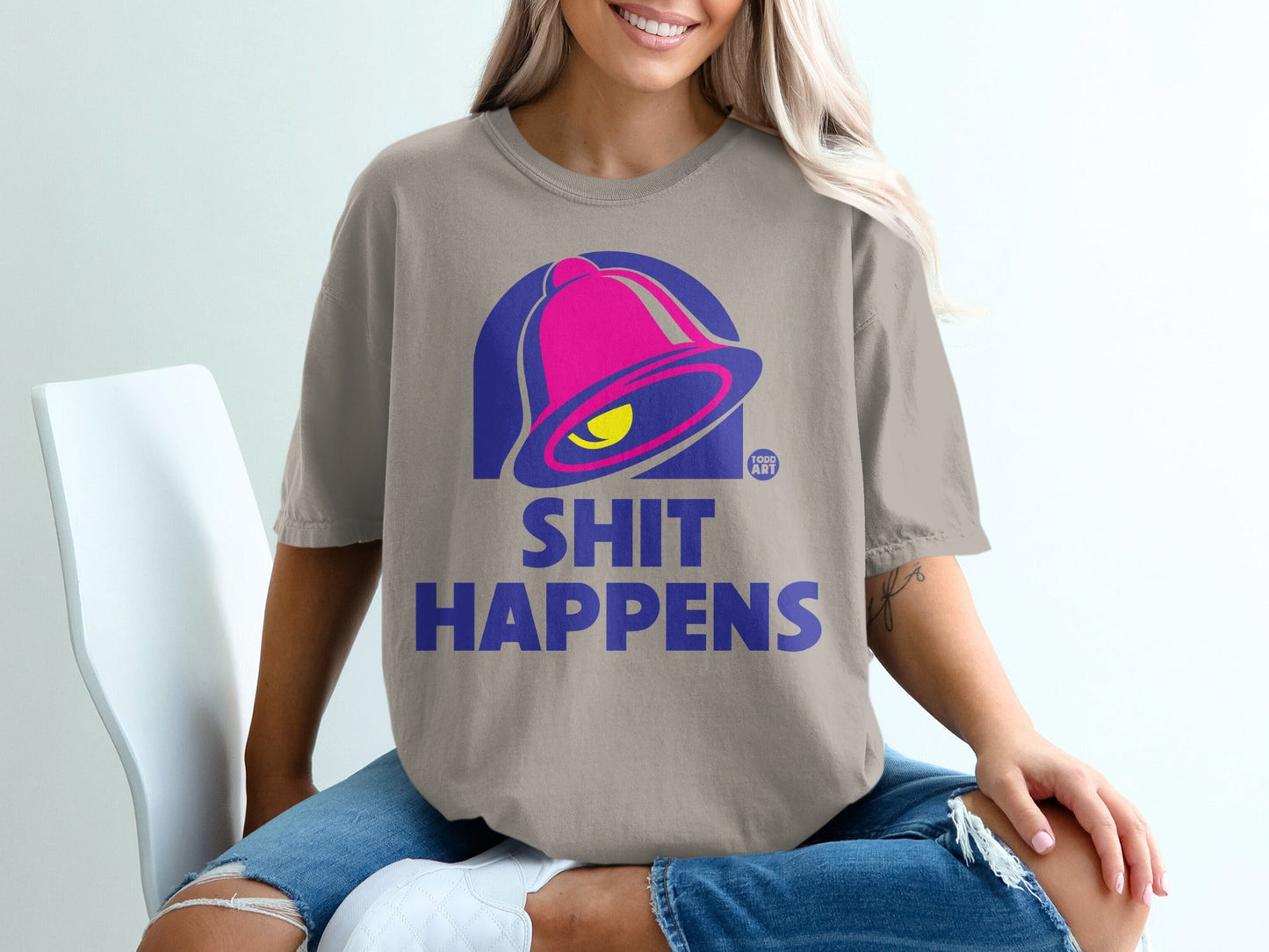 Bell graphic with "SHIT HAPPENS" text on a tan t-shirt.