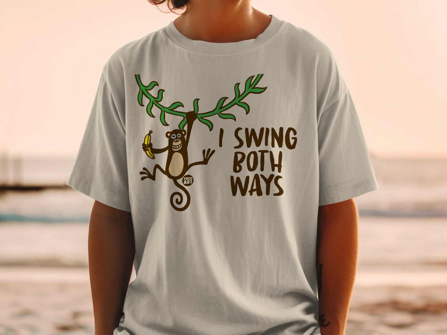T-shirt with brown monkey swinging from vine holding banana, text "I SWING BOTH WAYS".