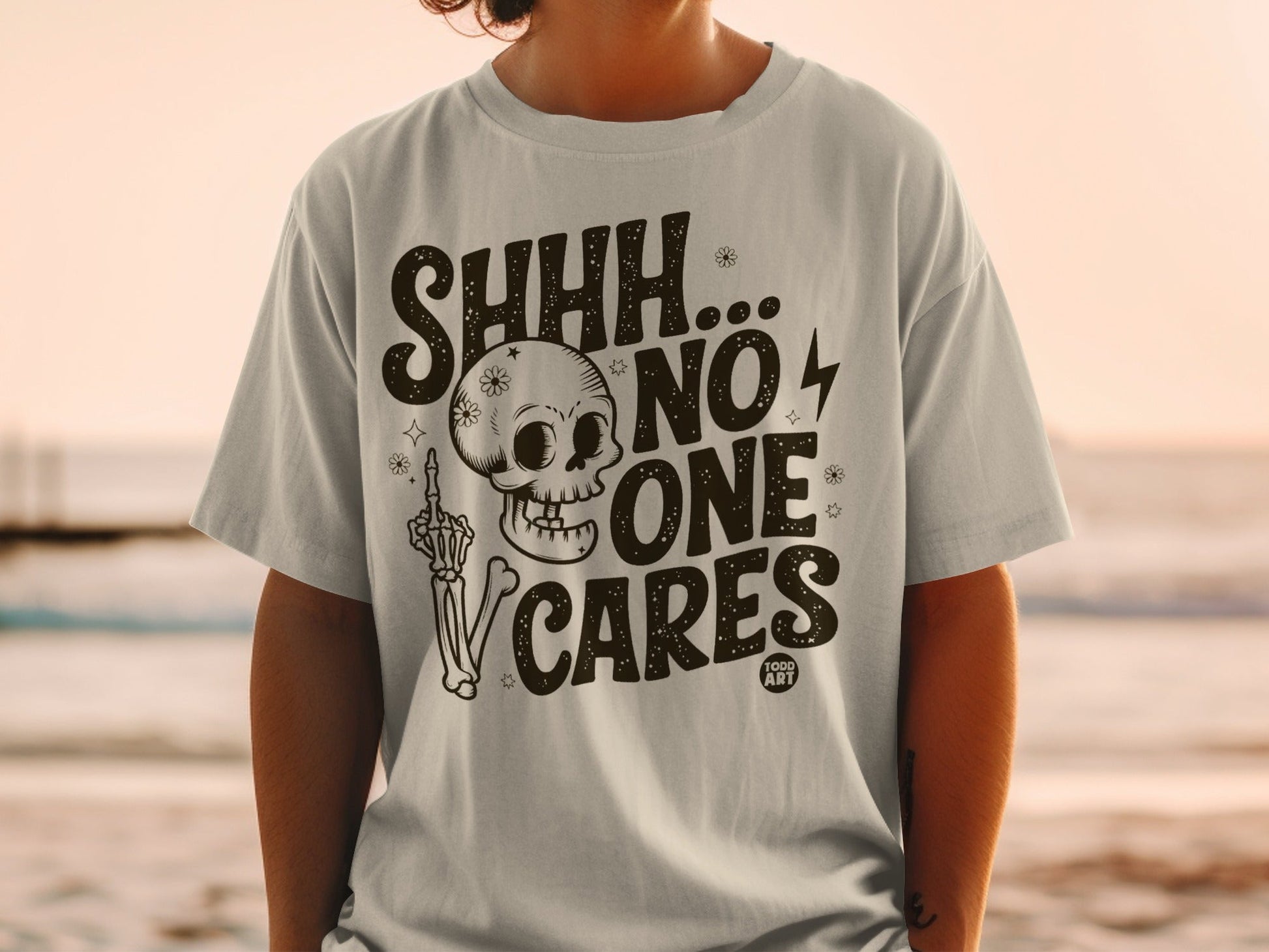 Light grey t-shirt with "SHHH... NO ONE CARES" and a skull with a skeleton hand.