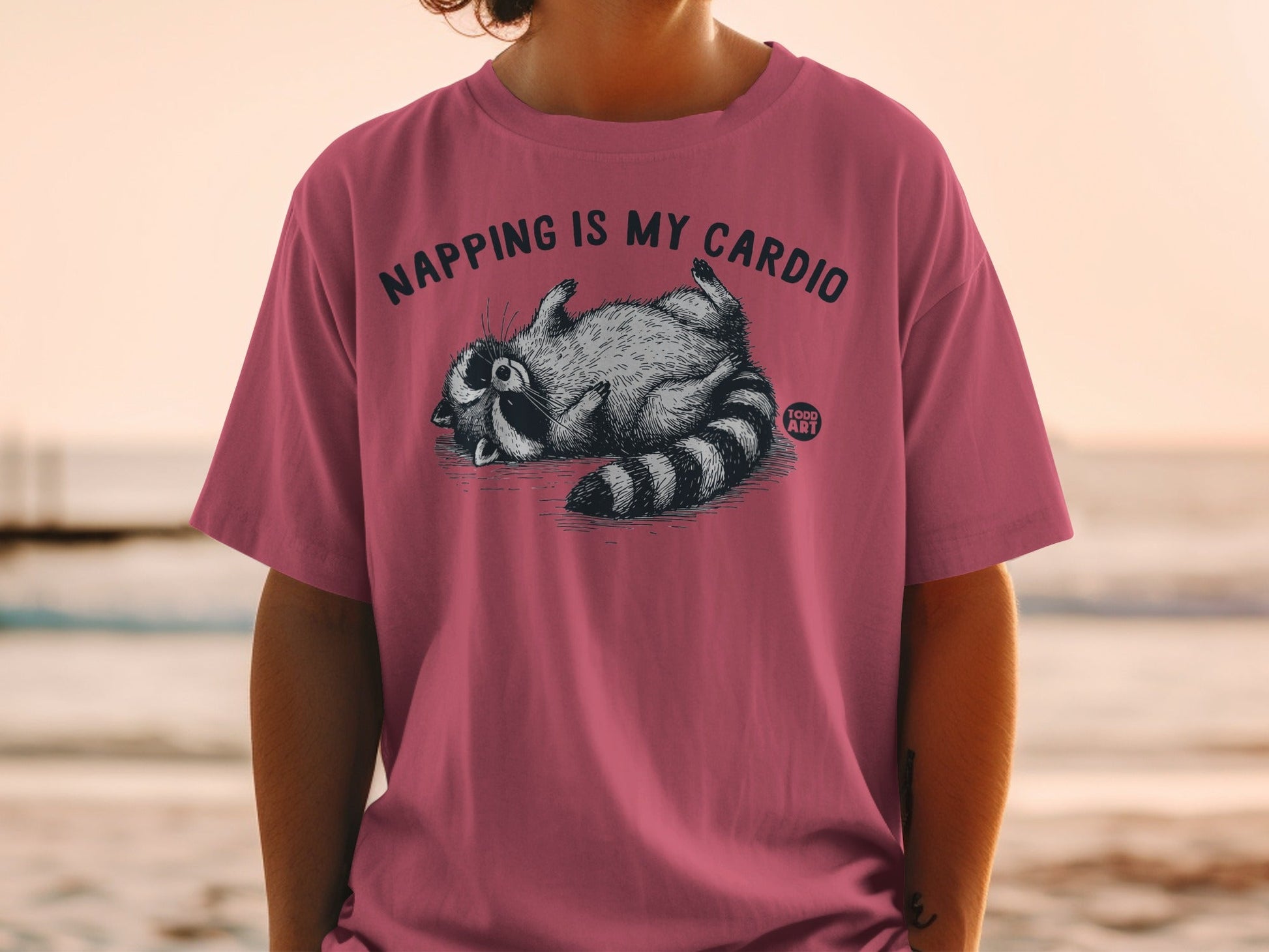 T-shirt with raccoon graphic and text "NAPPING IS MY CARDIO"