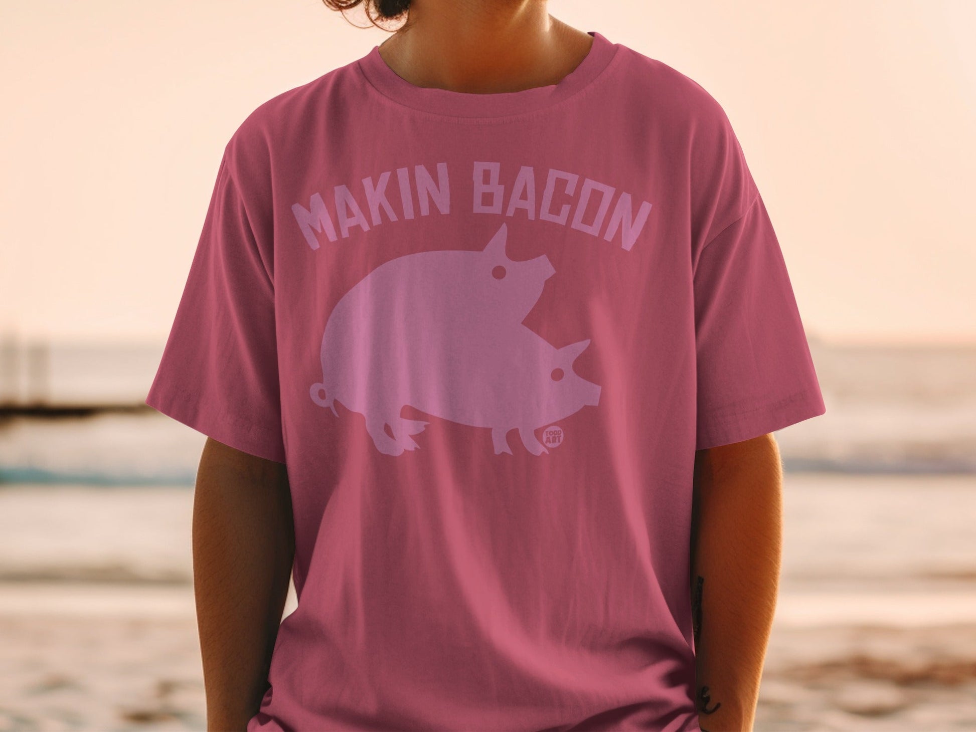 Pink t-shirt with "MAKIN' BACON" text and two pigs graphic.