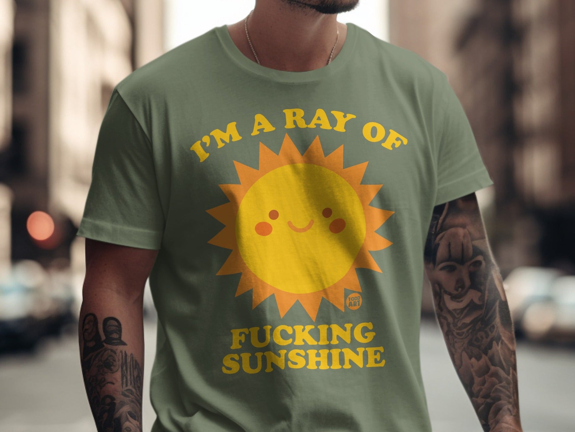 Olive green t-shirt with a smiling sun and "I'M A RAY OF FUCKING SUNSHINE" text.