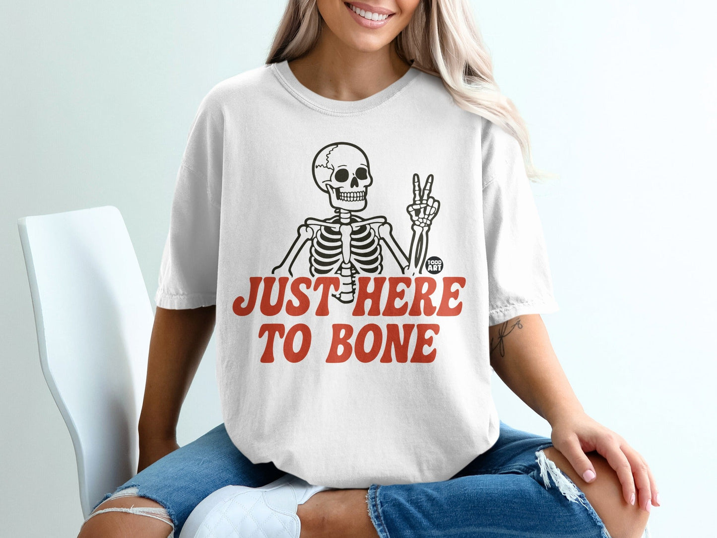 White t-shirt with skeleton graphic and "JUST HERE TO BONE" text.