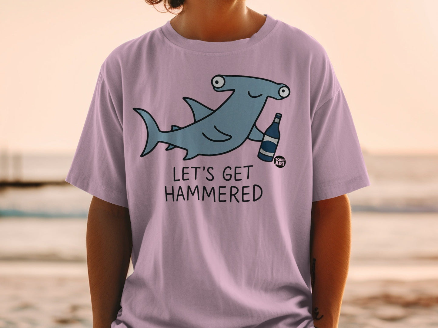 Light purple t-shirt with a cartoon hammerhead shark holding a bottle.