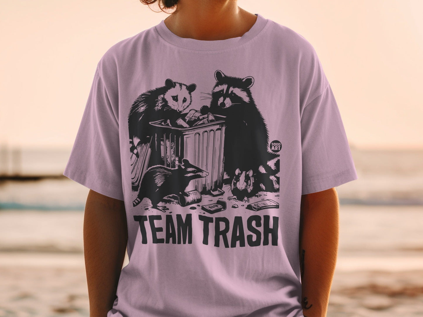 T-shirt graphic of raccoons digging through trash can with "TEAM TRASH" text.