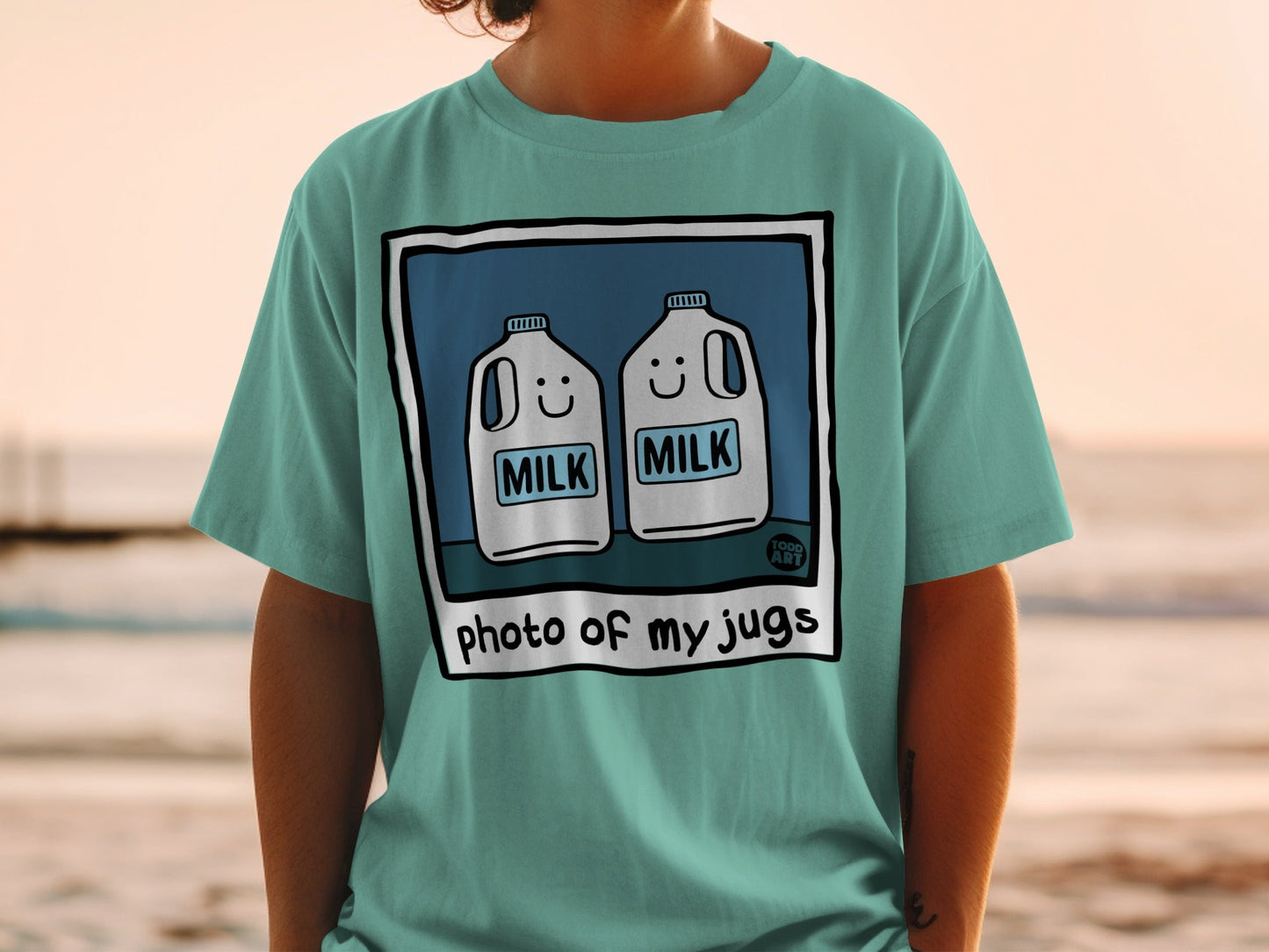 Two cartoon milk jugs with smiling faces on a teal t-shirt.