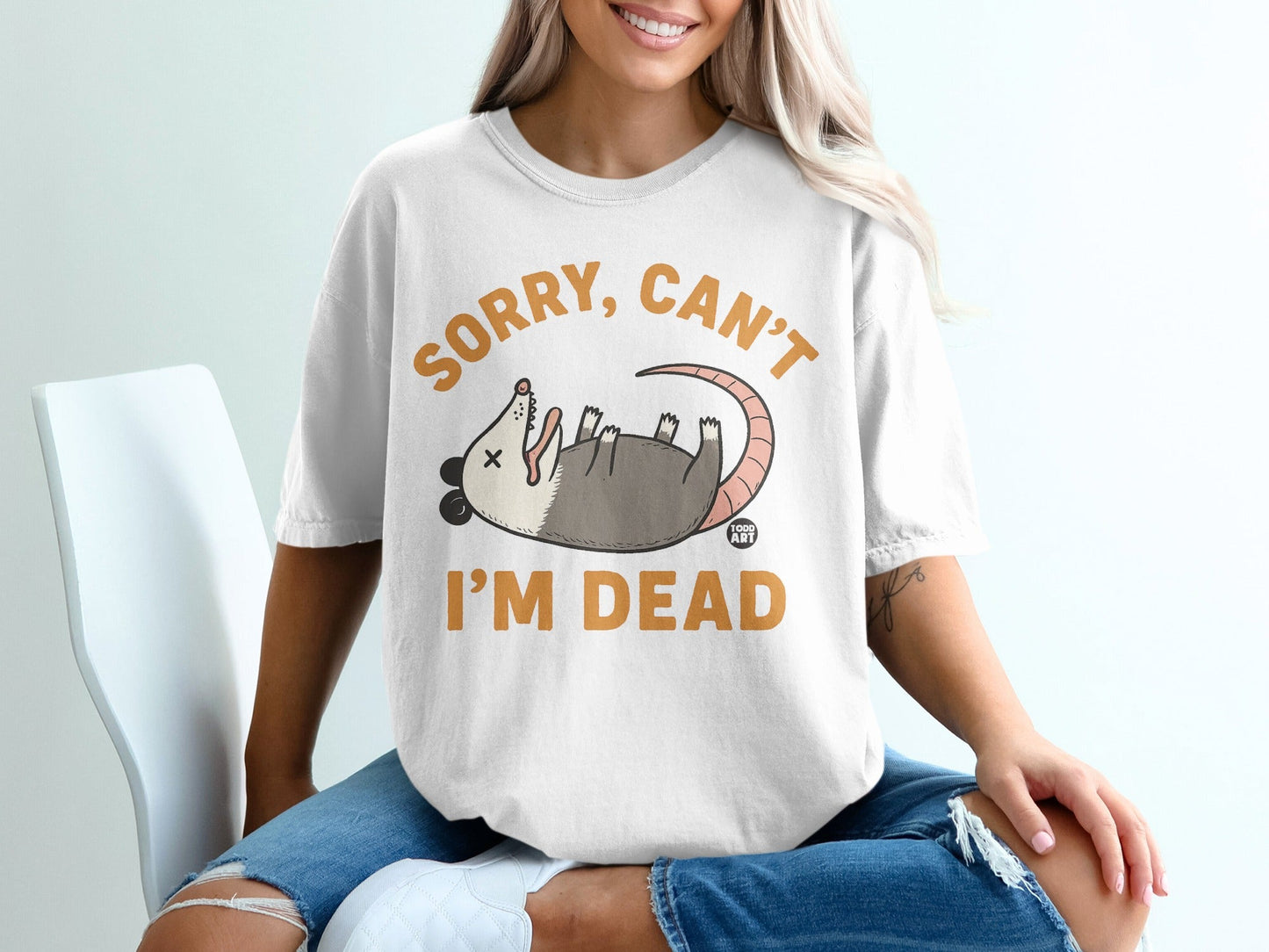 White t-shirt with a cartoon opossum and text that reads "SORRY, CAN'T I'M DEAD".