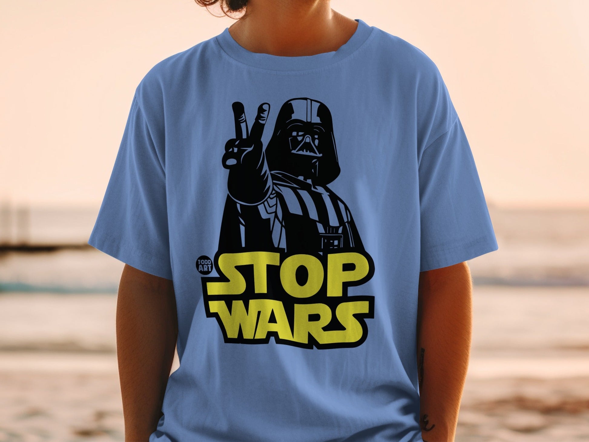 Darth Vader giving peace sign on blue t-shirt with "STOP WARS" text.